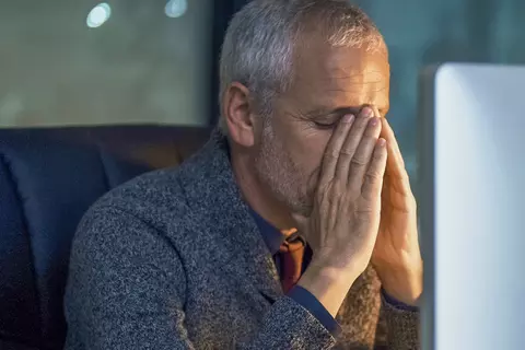 Ein Mann hält sich niedergeschlagen vor einem Bildschirm die Hand an die Stirn.