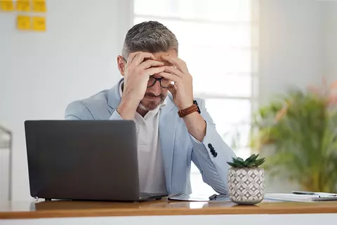Ein Mann sitzt vor seinem Laptop und stützt seinen Kopf mit den Händen ab