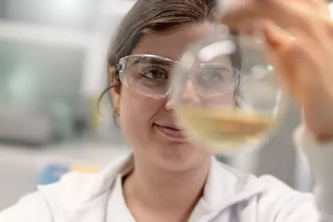 Nahaufnahme: Laborantin prüft eine Probe im Kolben im Laborumfeld.