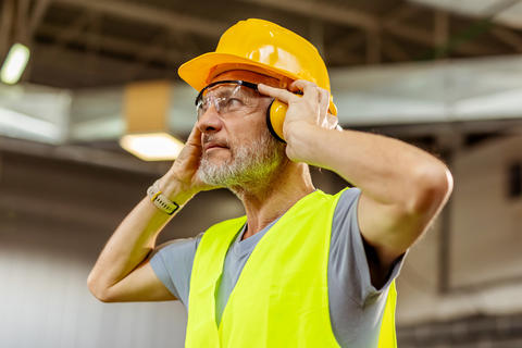 Arbeiter schützt sein Gehör mit Ohrschützern während der Arbeit in einem lauten Arbeitsumfeld.