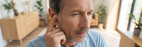 Mann mittleren Alters tippt nachdenklich mit dem Finger auf sein Ohr, möglicherweise aufgrund von Hörproblemen oder eines Tinnitus.