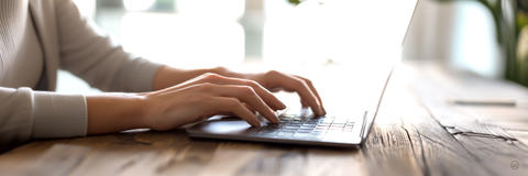 Nahaufnahme zweier Hände, die auf einer Laptop-Tastatur tippen.