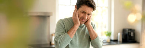 Leiden durch Ohrgeräusche: Mann greift sich mit beiden Händen verzweifelt an die Ohren.