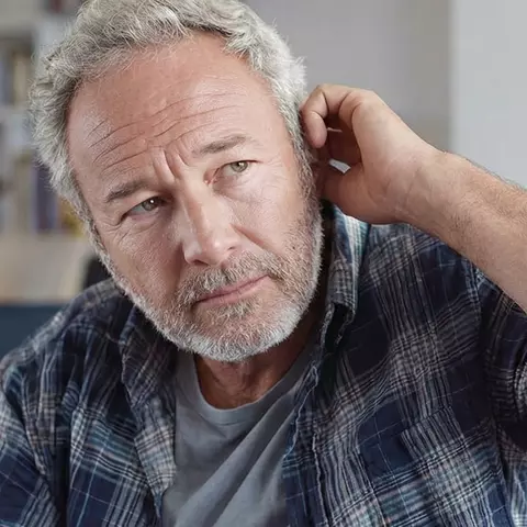 Mann mittleren Alters mit grauem Bart signalisiert Hörprobleme und spricht mit seinem Sohn.